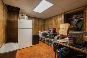 Kitchen featuring carpet floors, white fridge, a drop ceiling, and wood walls