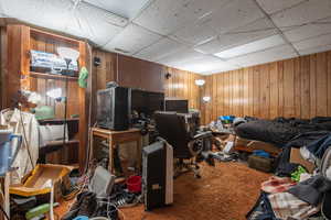 Home office with carpet, a drop ceiling, and wooden walls