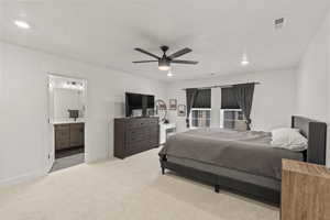 Master bedroom with ensuite bath, light colored carpet, and ceiling fan