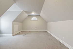 Additional living space featuring light carpet, vaulted ceiling, and a textured ceiling