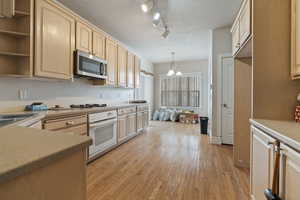 Kitchen with light brown cabinetry, hanging light fixtures, white appliances, a textured ceiling, and light wood-type flooring