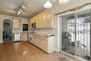 Kitchen featuring light brown cabinetry, decorative light fixtures, stainless steel appliances, a textured ceiling, and light wood-type flooring