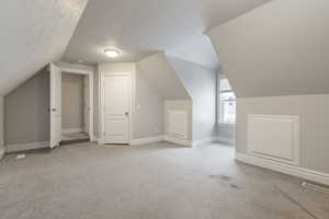 Additional living space with vaulted ceiling, light carpet, and a textured ceiling