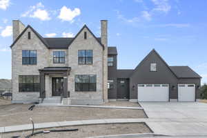 View of front facade with stone siding, concrete driveway, a standing seam roof, and a chimney