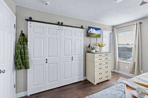 Bedroom featuring dark wood-type flooring, ceiling fan, a textured ceiling, a barn door, and a closet