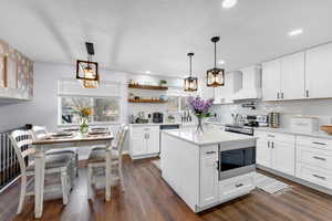 Kitchen with built in microwave, stainless steel electric range, pendant lighting, wall chimney range hood, and white cabinets