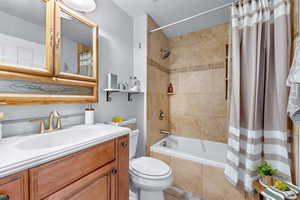 Full bathroom with shower / bathtub combination with curtain, vanity, a textured ceiling, and toilet