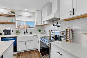 Kitchen with sink, dishwasher, white cabinetry, custom range hood, and stainless steel range with electric cooktop