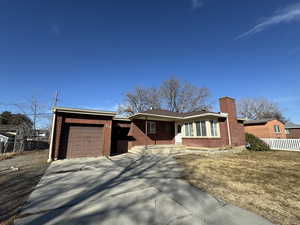 Single story home featuring a garage, brick siding, fence, concrete driveway, and a chimney