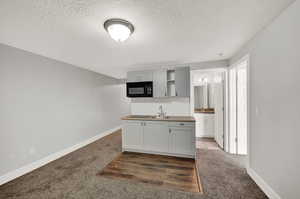 Kitchen featuring sink, dark carpet, gray cabinets, and a textured ceiling