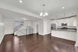 Kitchen featuring hanging light fixtures, appliances with stainless steel finishes, dark wood-type flooring, and white cabinets