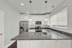 Kitchen featuring stainless steel appliances, white cabinetry, hanging light fixtures, and dark stone counters