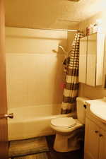 Full bathroom featuring hardwood / wood-style floors, vanity, toilet, shower / bath combo, and a textured ceiling