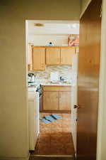 Kitchen featuring light brown cabinetry, sink, backsplash, and stainless steel range oven