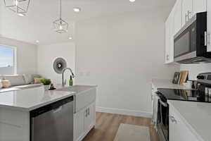 Kitchen with sink, white cabinetry, stainless steel appliances, decorative light fixtures, and light wood-type flooring