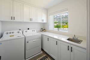 Clothes washing area featuring sink, washer and clothes dryer, cabinets, and dark tile patterned flooring