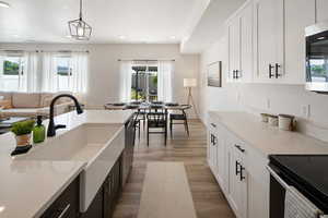 Kitchen with dark hardwood / wood-style floors, decorative light fixtures, white cabinets, electric range, and light stone counters