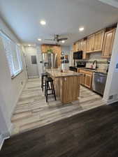 Kitchen with sink, a center island, appliances with stainless steel finishes, light stone countertops, and light hardwood / wood-style floors