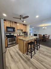 Kitchen with a kitchen island, appliances with stainless steel finishes, sink, a kitchen bar, and light wood-type flooring