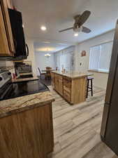 Kitchen featuring appliances with stainless steel finishes, hanging light fixtures, a center island, light hardwood / wood-style floors, and light stone countertops