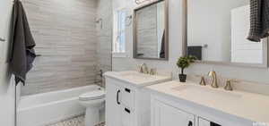 Fully remodeled bathroom with vanity, toilet, and tiled shower / bath and double sinks