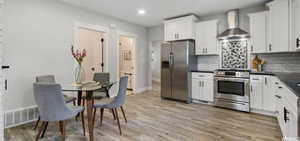 Kitchen featuring appliances with stainless steel finishes, white cabinetry, decorative backsplash, wall chimney range hood, and light hardwood / wood-style flooring