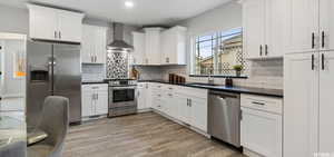 Kitchen with sink, stainless steel appliances, white cabinets, and wall chimney exhaust hood