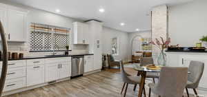 Kitchen with sink, white cabinetry, stainless steel dishwasher, light hardwood / wood-style floors, and backsplash