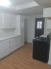 Kitchen with gas range, white dishwasher, white cabinetry, and light wood finished floors