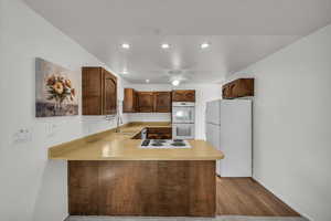 Kitchen featuring sink, white appliances, light wood-type flooring, kitchen peninsula, and ceiling fan