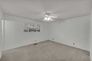 Unfurnished room featuring ceiling fan, light colored carpet, and a textured ceiling