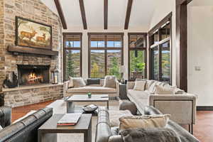 Living room featuring wood-type flooring, a wealth of natural light, a stone fireplace, and vaulted ceiling with beams