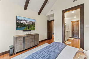 Bedroom featuring light wood-type flooring, vaulted ceiling with beams, and ensuite bath