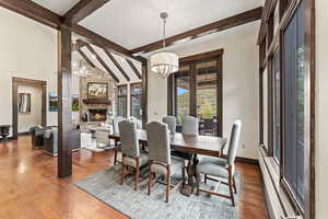 Dining space featuring an inviting chandelier, lofted ceiling with beams, a stone fireplace, and dark hardwood / wood-style flooring