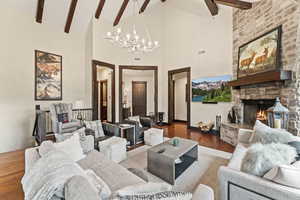 Living room featuring beamed ceiling, a stone fireplace, hardwood / wood-style floors, high vaulted ceiling, and an inviting chandelier