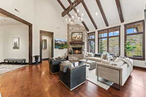 Living room featuring high vaulted ceiling, beamed ceiling, dark wood-type flooring, and a stone fireplace