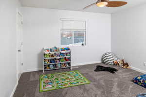 Recreation room with ceiling fan and dark carpet