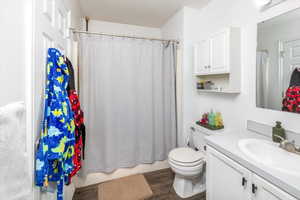 Full bathroom with hardwood / wood-style flooring, vanity, shower / bath combo, and toilet