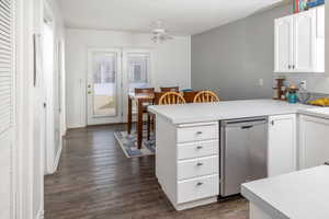 Kitchen featuring stainless steel dishwasher, dark hardwood / wood-style floors, kitchen peninsula, ceiling fan, and white cabinets