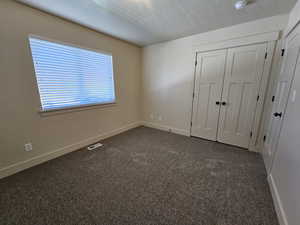 Unfurnished bedroom with a textured ceiling, a closet, and dark colored carpet