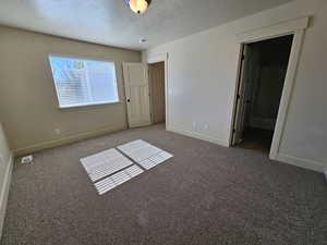 Unfurnished bedroom with ensuite bathroom, a textured ceiling, and dark colored carpet