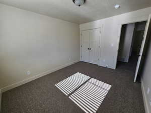 Unfurnished bedroom featuring a textured ceiling, a closet, and dark colored carpet