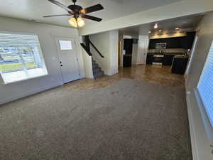 Unfurnished living room featuring ceiling fan, dark tile patterned flooring, sink, and a textured ceiling