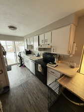 Kitchen featuring a textured ceiling, white cabinets, black range with electric cooktop, stainless steel dishwasher, and white fridge