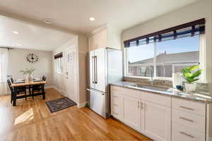 Kitchen featuring stone countertops, white cabinetry, sink, stainless steel fridge, and light wood-type flooring