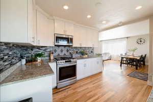 Kitchen with light hardwood / wood-style flooring, stone counters, backsplash, stainless steel appliances, and white cabinets