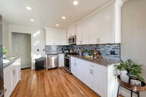 Kitchen featuring stone counters, appliances with stainless steel finishes, white cabinets, decorative backsplash, and light hardwood / wood-style flooring