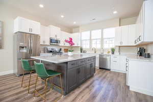 Kitchen featuring a kitchen island, white cabinetry, a breakfast bar area, stainless steel appliances, and light wood-type flooring