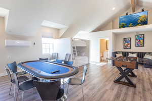 Rec room featuring lofted ceiling with beams, a wall unit AC, and light hardwood / wood-style flooring