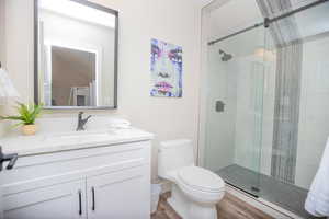 Bathroom with hardwood / wood-style flooring, vanity, an enclosed shower, and toilet